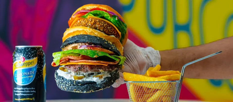 Close-up of gourmet burgers with black buns, served with fries and a lemonade can.